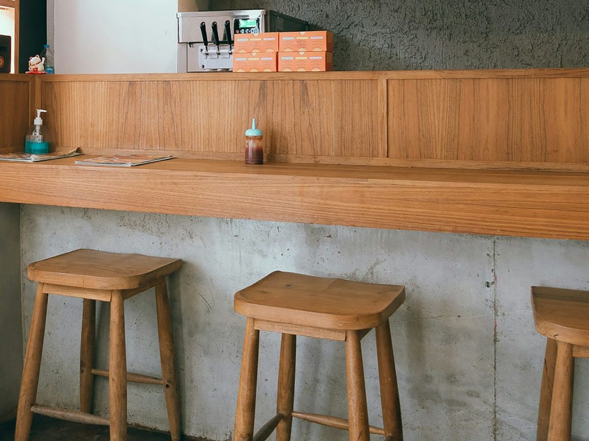 A long timber counter with simple wooden stools against a concrete base.