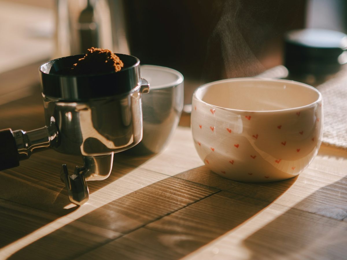 Coffee and a portafilter on a timber table in strong morning light and shadow.
