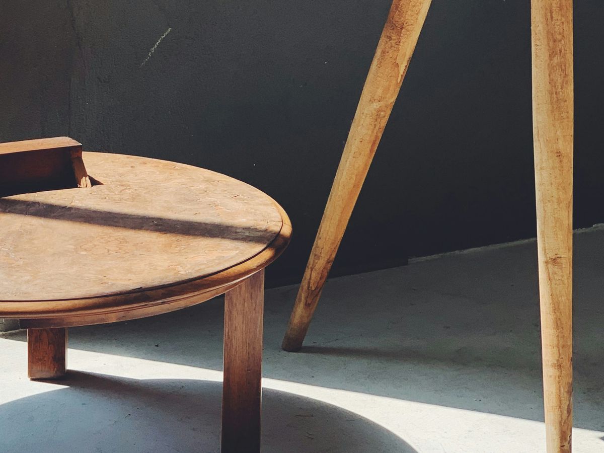 A round timber stool and splayed table legs casting soft shadows on a concrete floor.