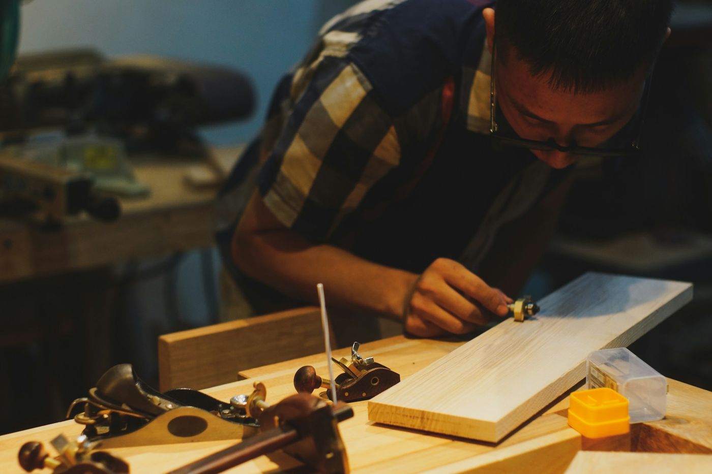 A maker hand-finishing a timber board at a workbench surrounded by hand planes.